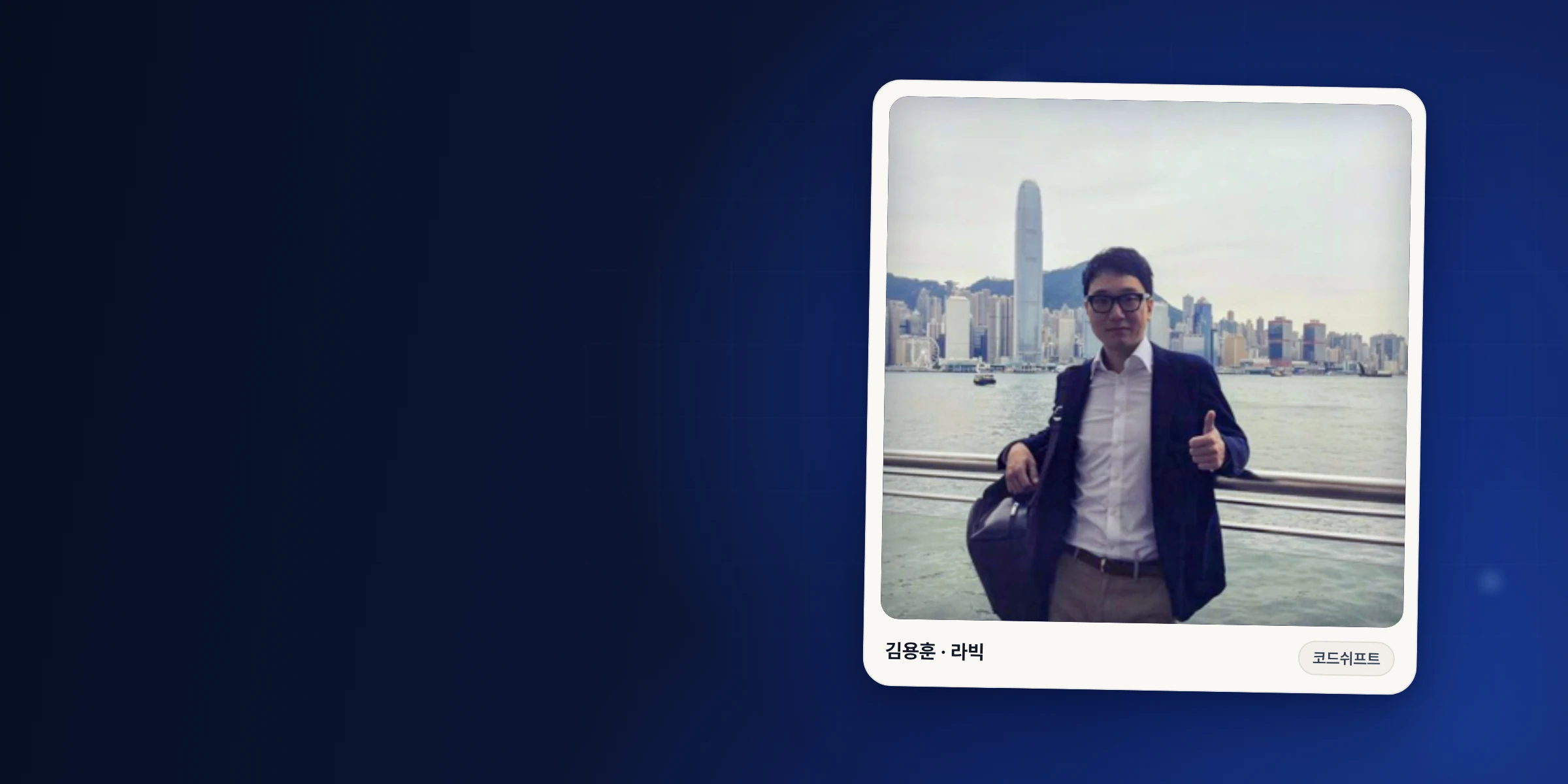 안경을 쓰고 흰 셔츠와 남색 재킷을 입은 김용훈이 바다와 고층 빌딩을 배경으로 난간 앞에 서서, 한쪽 어깨에 가방을 메고 다른 손으로 엄지를 들어 보이는 사진.